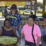 Three people holding corn and watermelon at the Ottawa County Farmer's Market