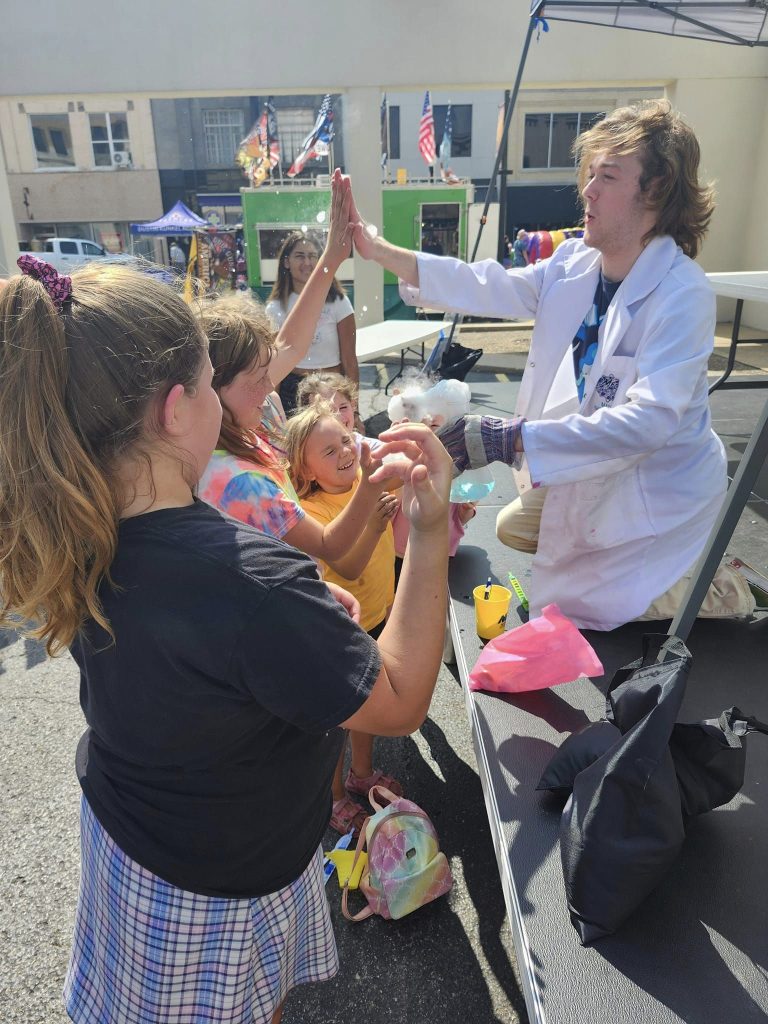 two older elementary age girls giving a high-five to a man dressed as a scientist